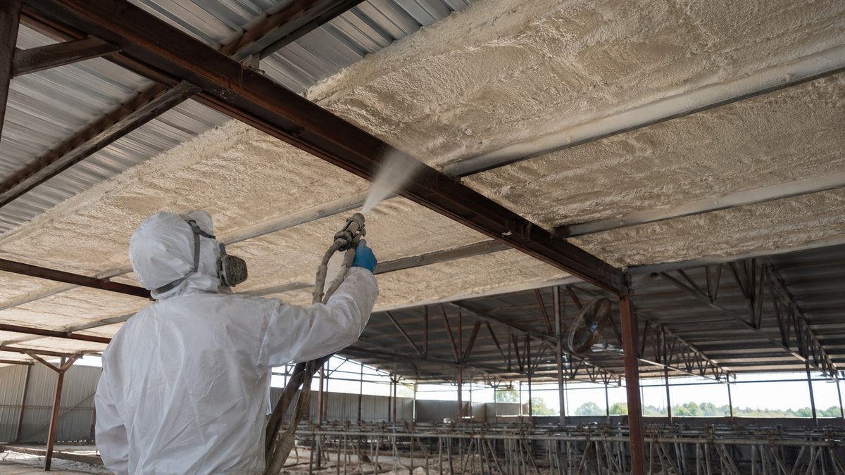 Operator spraying polyurethane foam insulation inside a livestock barn