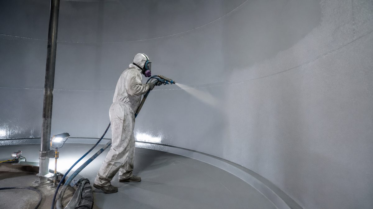 Worker spray-applying NSF-grade polyurea lining inside a potable water tank